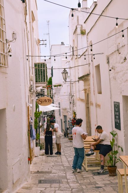 Explore a cozy street scene in Ostuni, Italy featuring charming cafes and historic architecture.