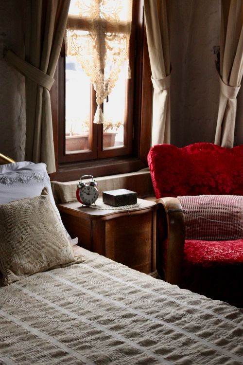 Free A vintage bedroom featuring a red armchair, lace curtains, and an antique alarm clock in warm lighting. Stock Photo