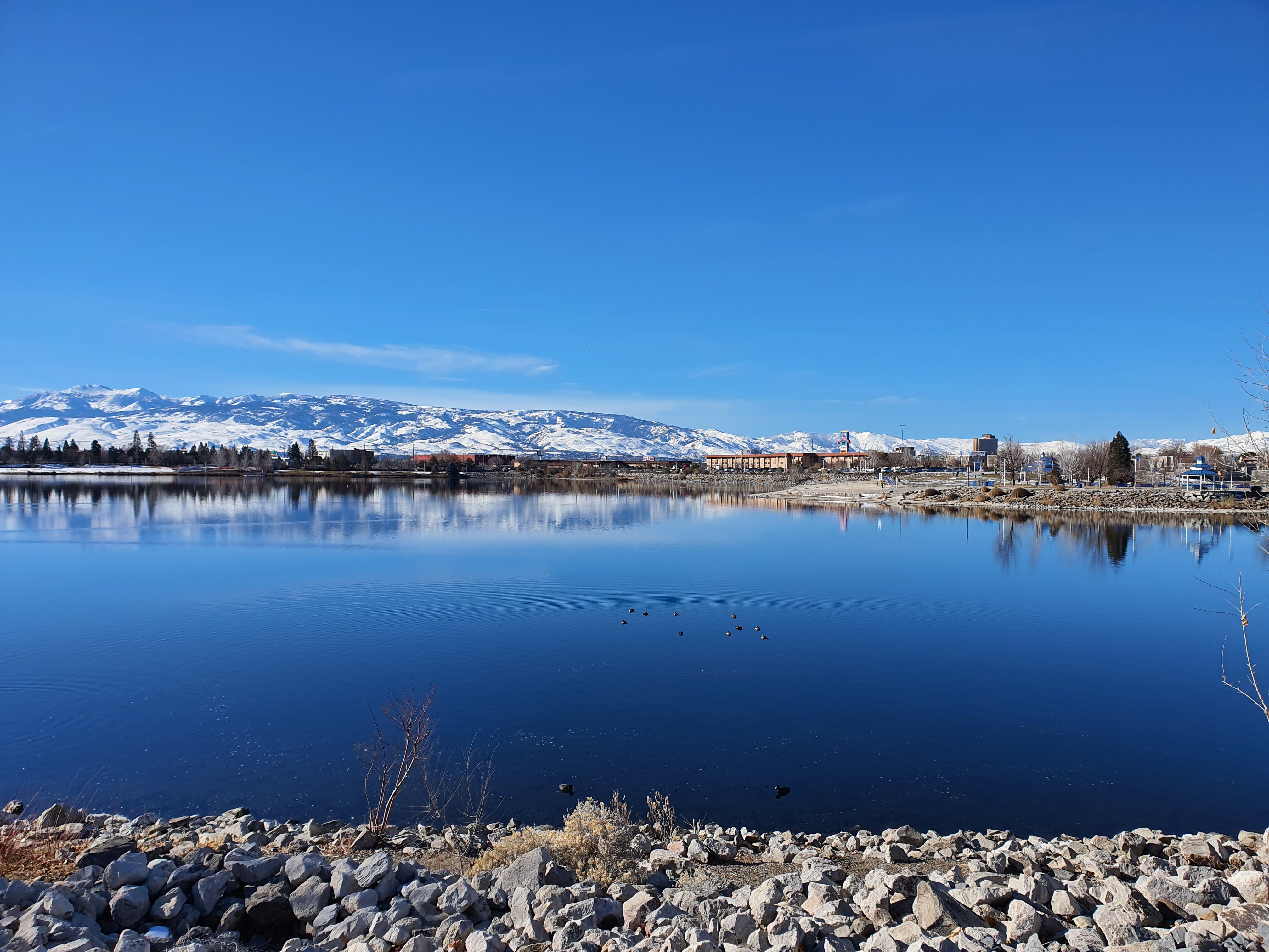A tranquil winter lake scene reflecting the snowy Sierra Nevada mountains under clear blue skies.