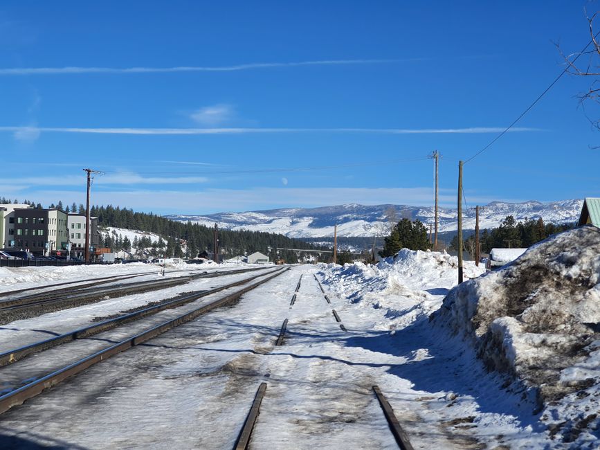 Winter scene of snow-covered railroad tracks in Truckee, California, with mountains in the background.