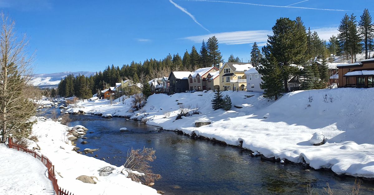 Charming winter scene in Truckee with snow-covered homes along the Truckee River under a bright blue sky.