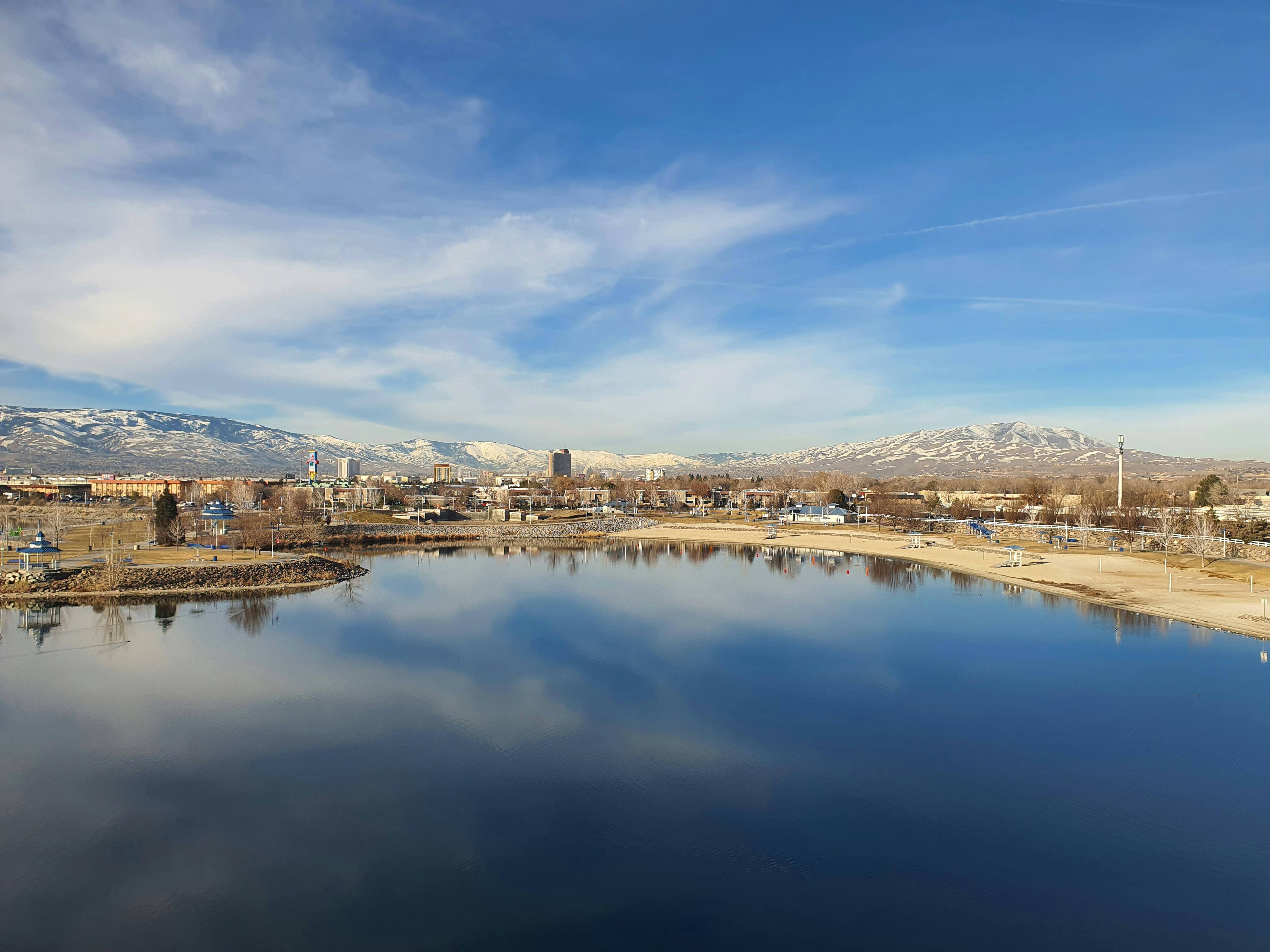 Discover Reno's skyline reflecting on a tranquil lake with snow-capped Sierra Nevada mountains in the background.
