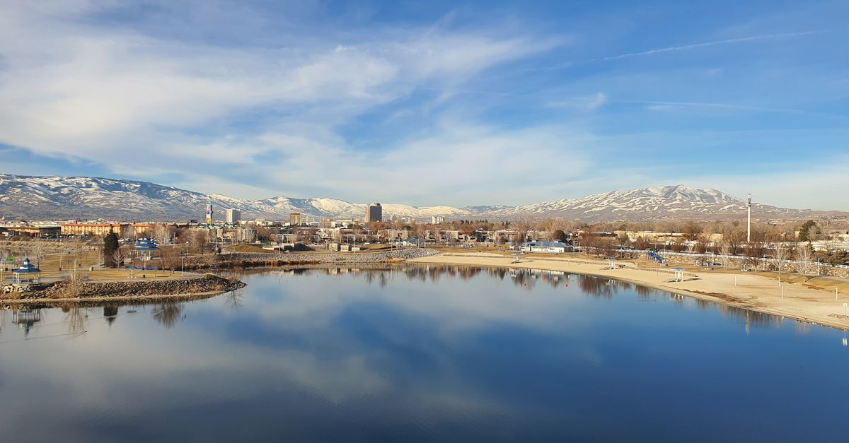 Discover Reno's skyline reflecting on a tranquil lake with snow-capped Sierra Nevada mountains in the background.