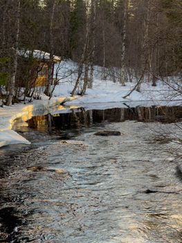 A serene snowy stream in Sinettä, Finland with a cabin nearby, captured at sunset.