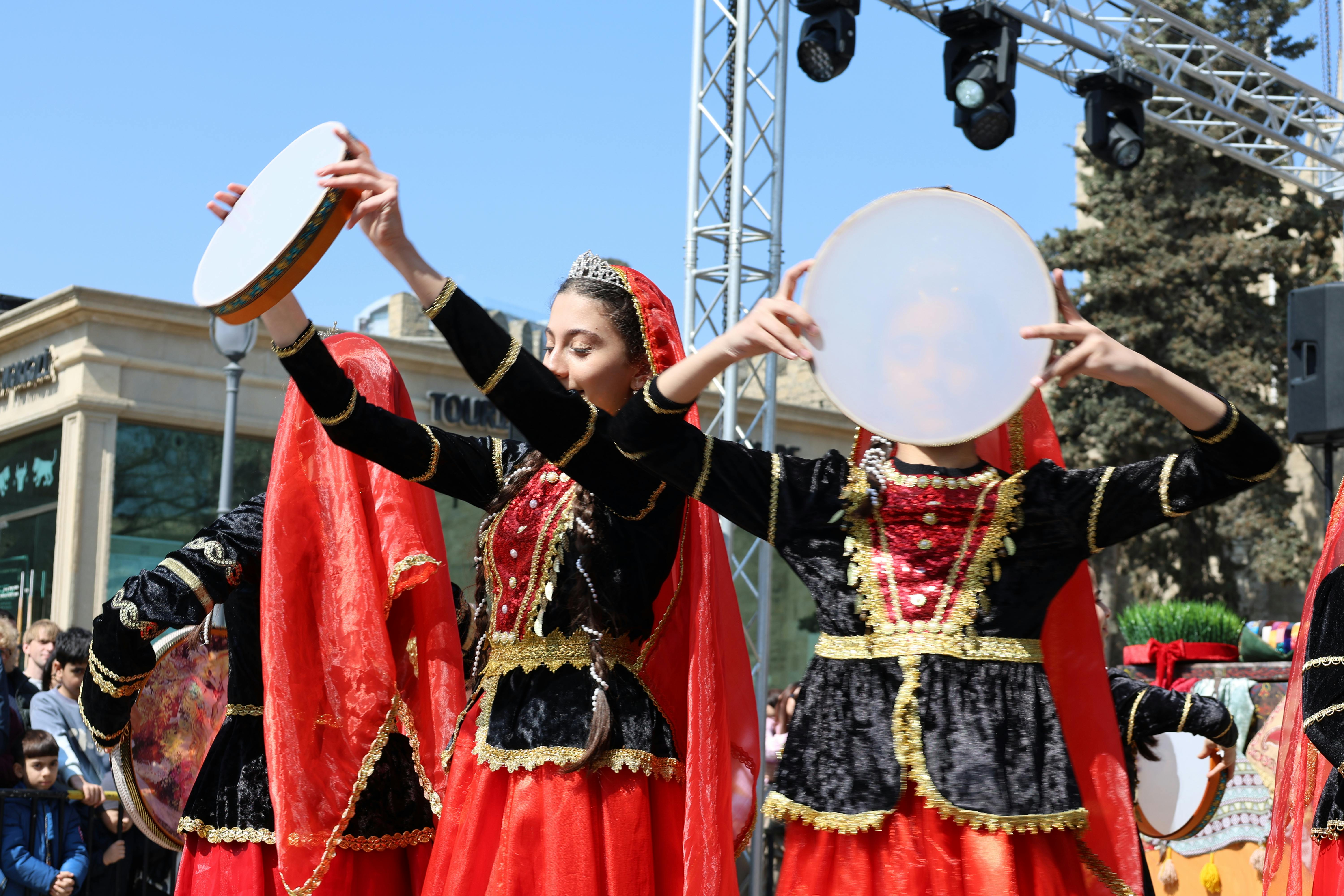Colorful traditional dancers with tambourines during a lively outdoor performance under sunny skies.