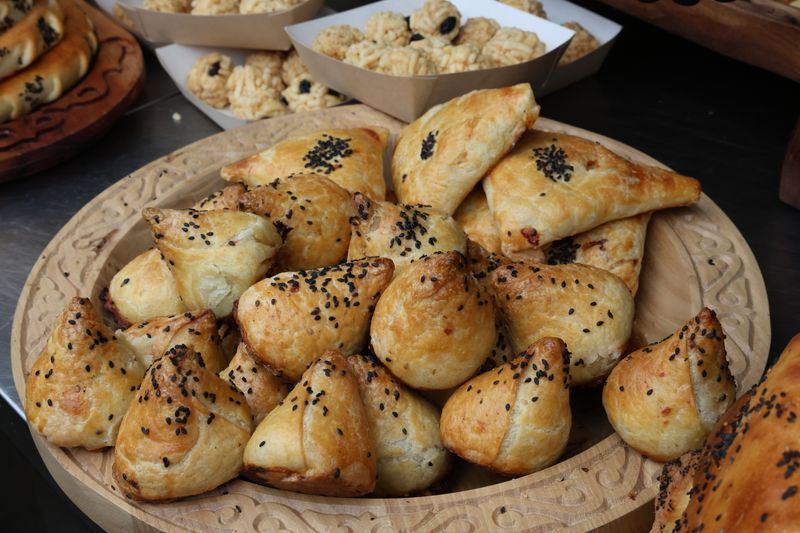 Freshly baked pastries with sesame seeds displayed on a wooden plate.