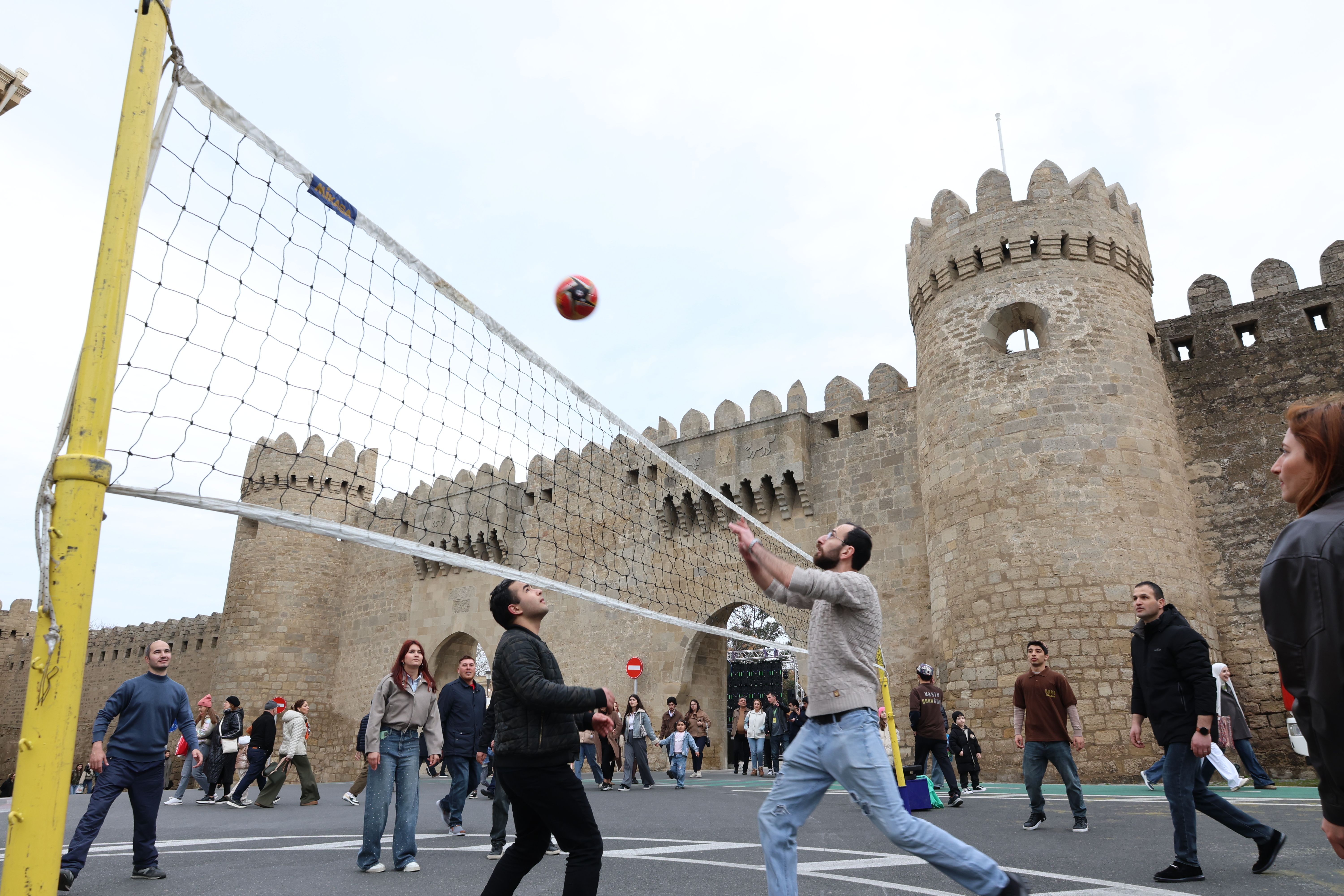 Free Group playing volleyball near an ancient castle wall, capturing the blend of sports and history. Stock Photo