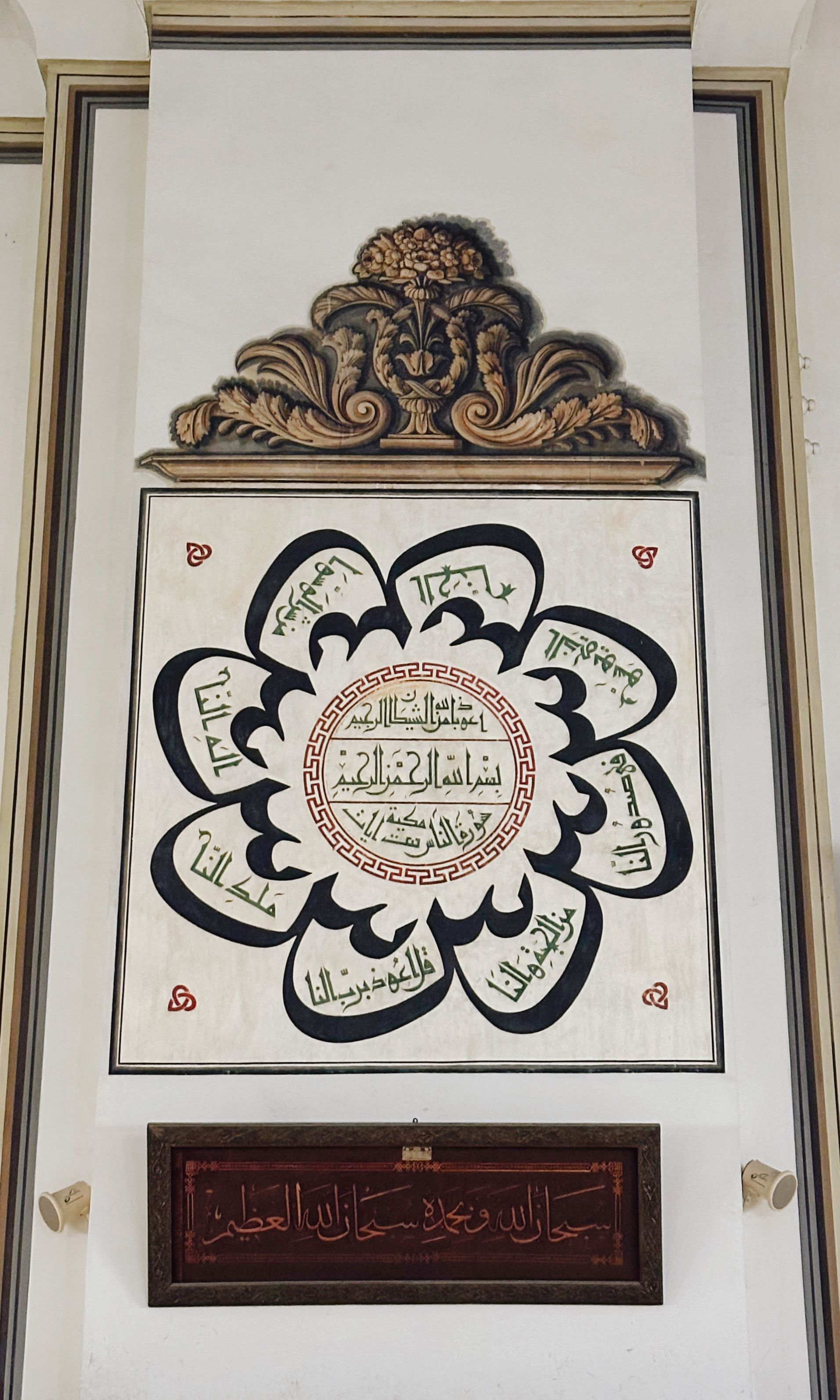 Ornate Islamic calligraphy framed with intricate carvings on a wall, showcasing artistic design.