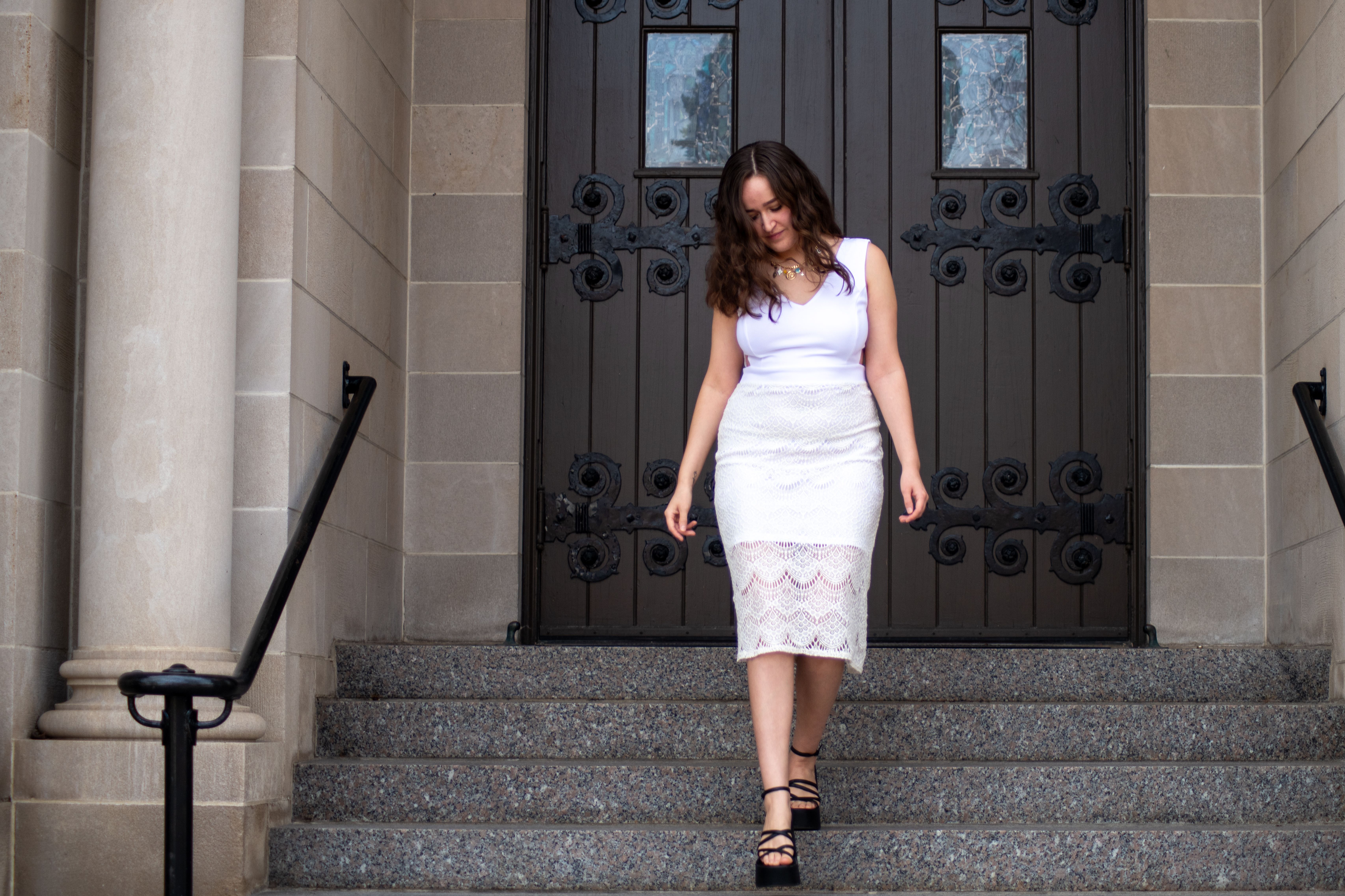 A young woman in a white dress descends steps in front of a church entrance.