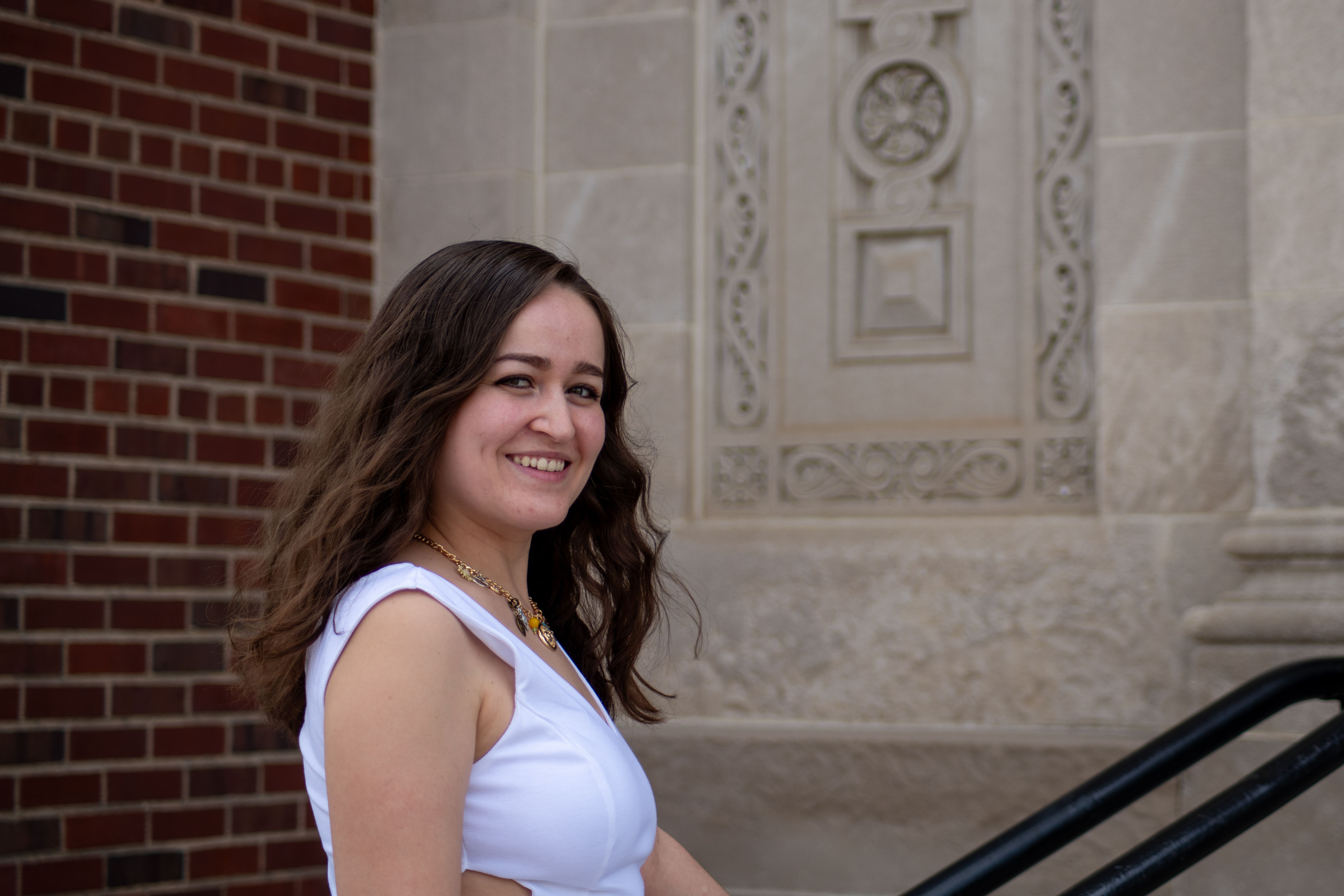 Smiling young woman in a white dress outside a historic stone building.