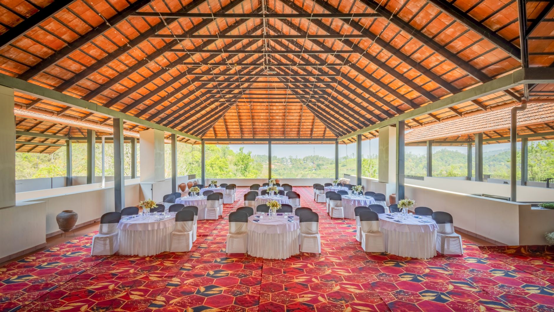 Spacious outdoor venue set for an event with decorated tables under a wooden roof.