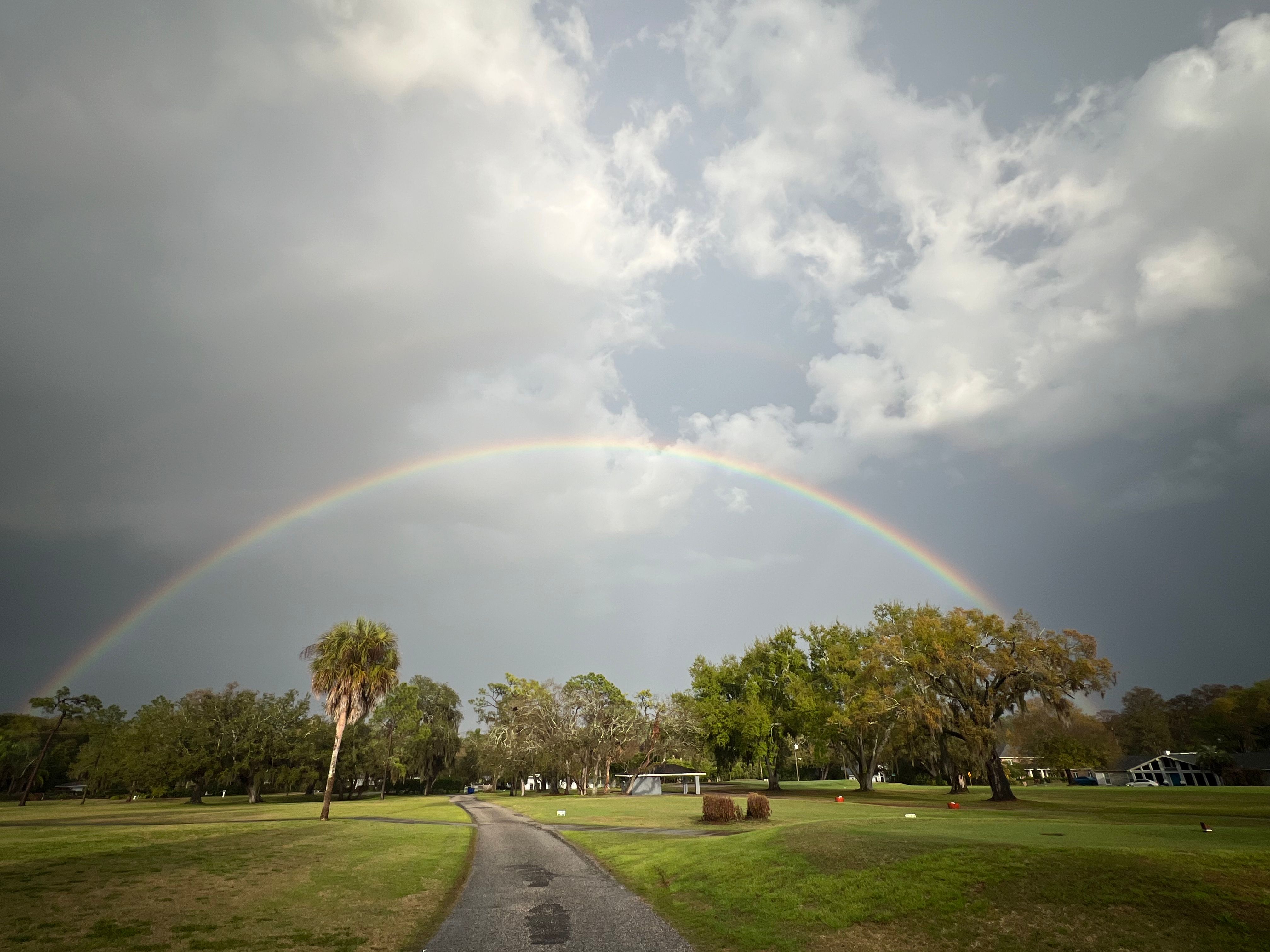 A brilliant rainbow arches over a tranquil golf course, creating a picturesque scene in a tropical landscape.