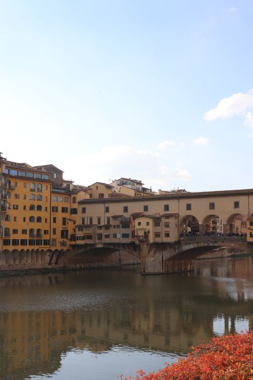 Free Scenic view of Ponte Vecchio in Florence reflecting on the Arno River under a clear sky. Stock Photo