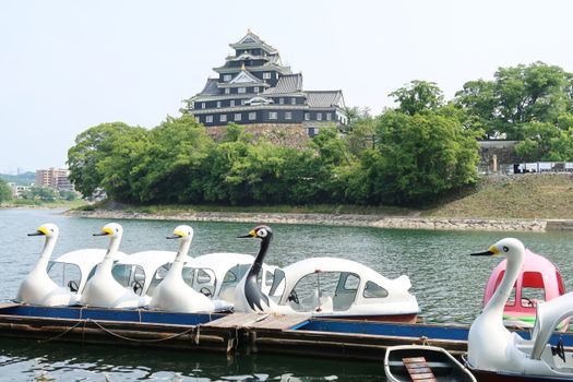 Swan-shaped boats on Asahi River with Okayama Castle in the background, Japan.