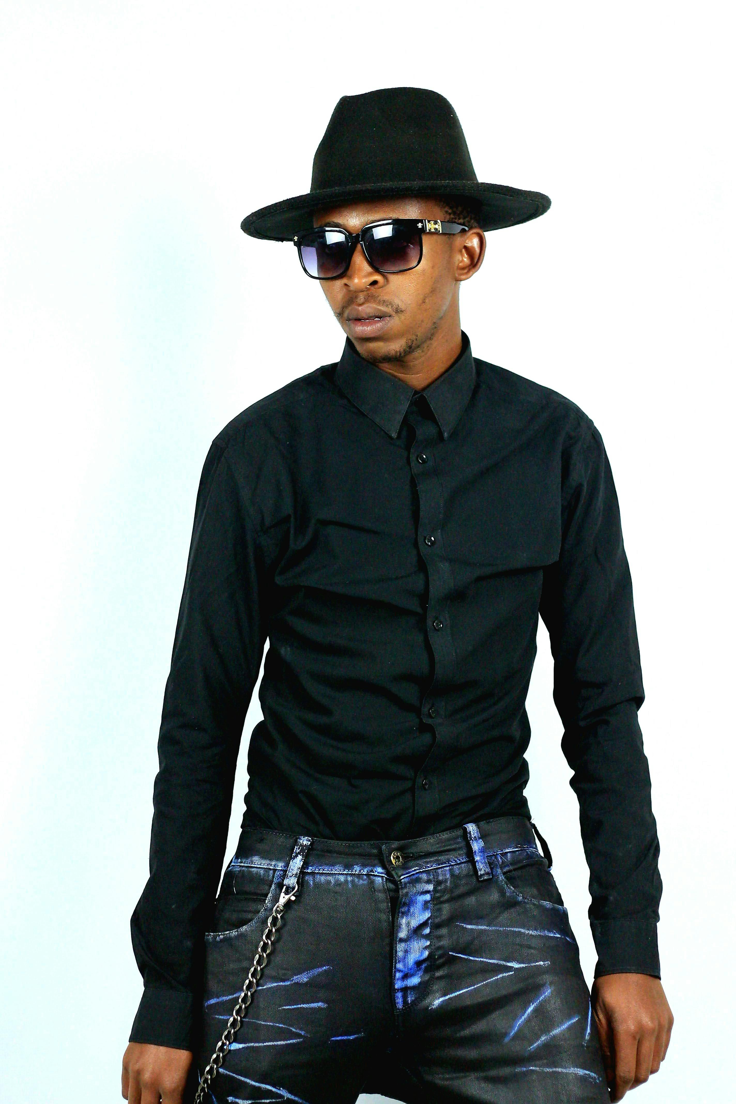 Fashionable man wearing a black shirt, fedora, and sunglasses against a plain background.