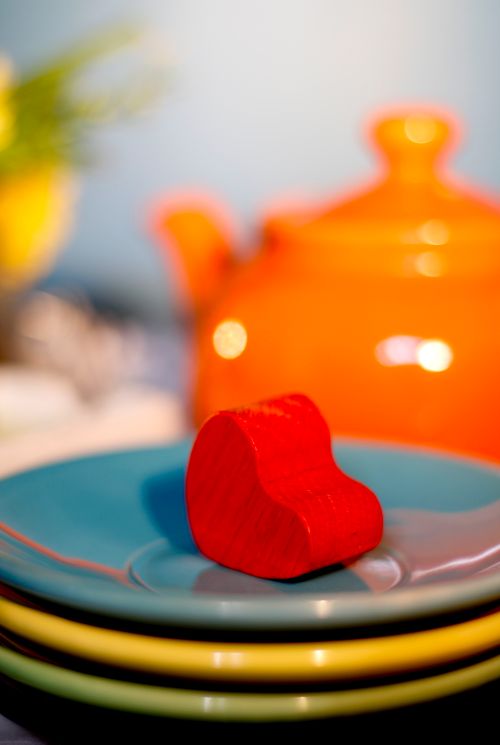 Free Stylish table setup featuring a red heart block, colorful plates, and an orange teapot. Stock Photo