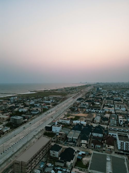 Free Aerial view of a coastal cityscape with buildings and roads under a pink sunset sky. Stock Photo