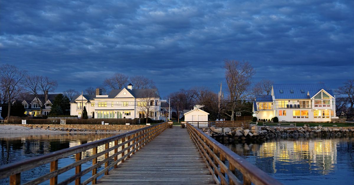 A tranquil pier extends into twilight, with waterfront homes glowing in Norwalk, Connecticut.