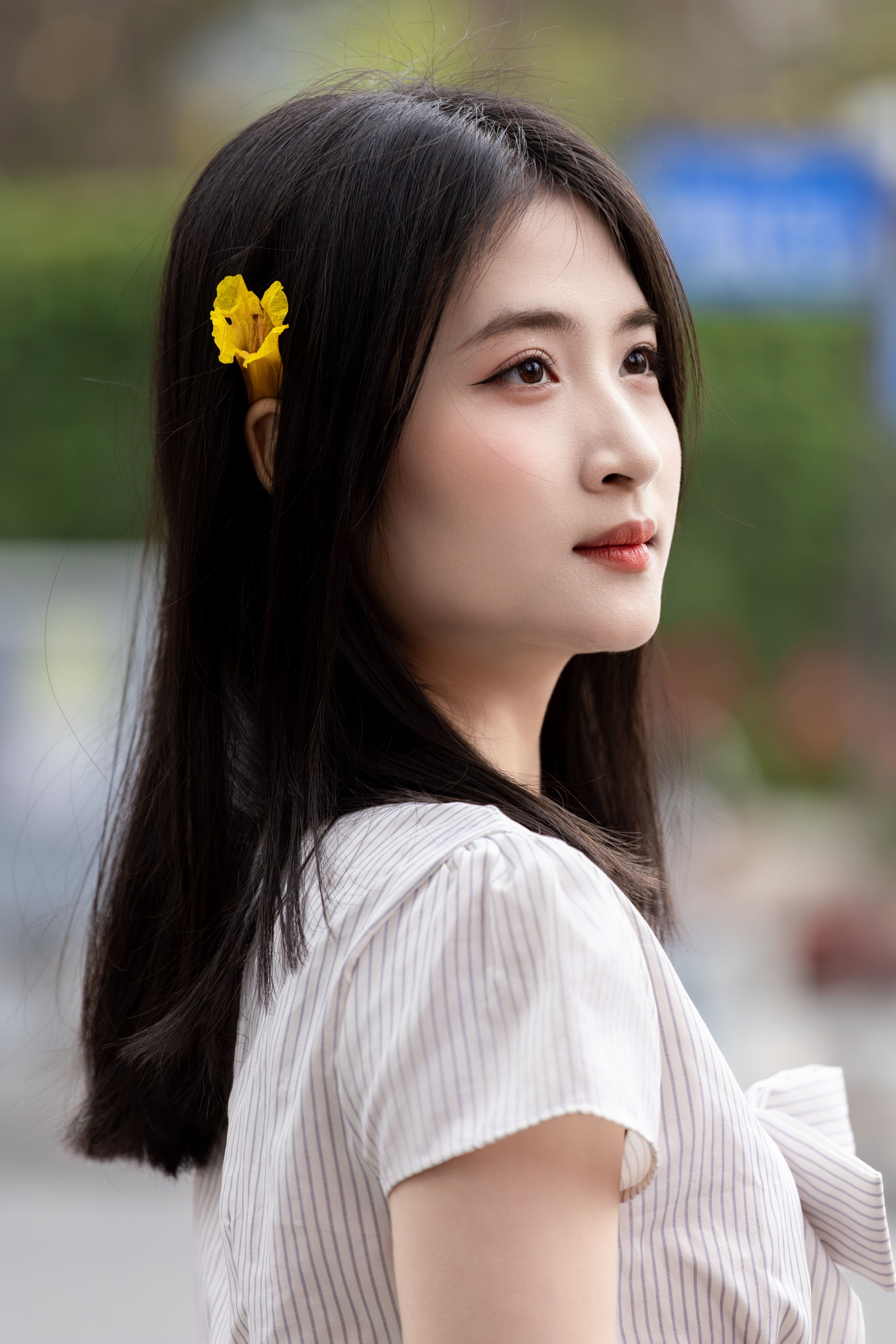 Side profile portrait of a woman with a yellow flower in her hair, taken outdoors in Hanoi.