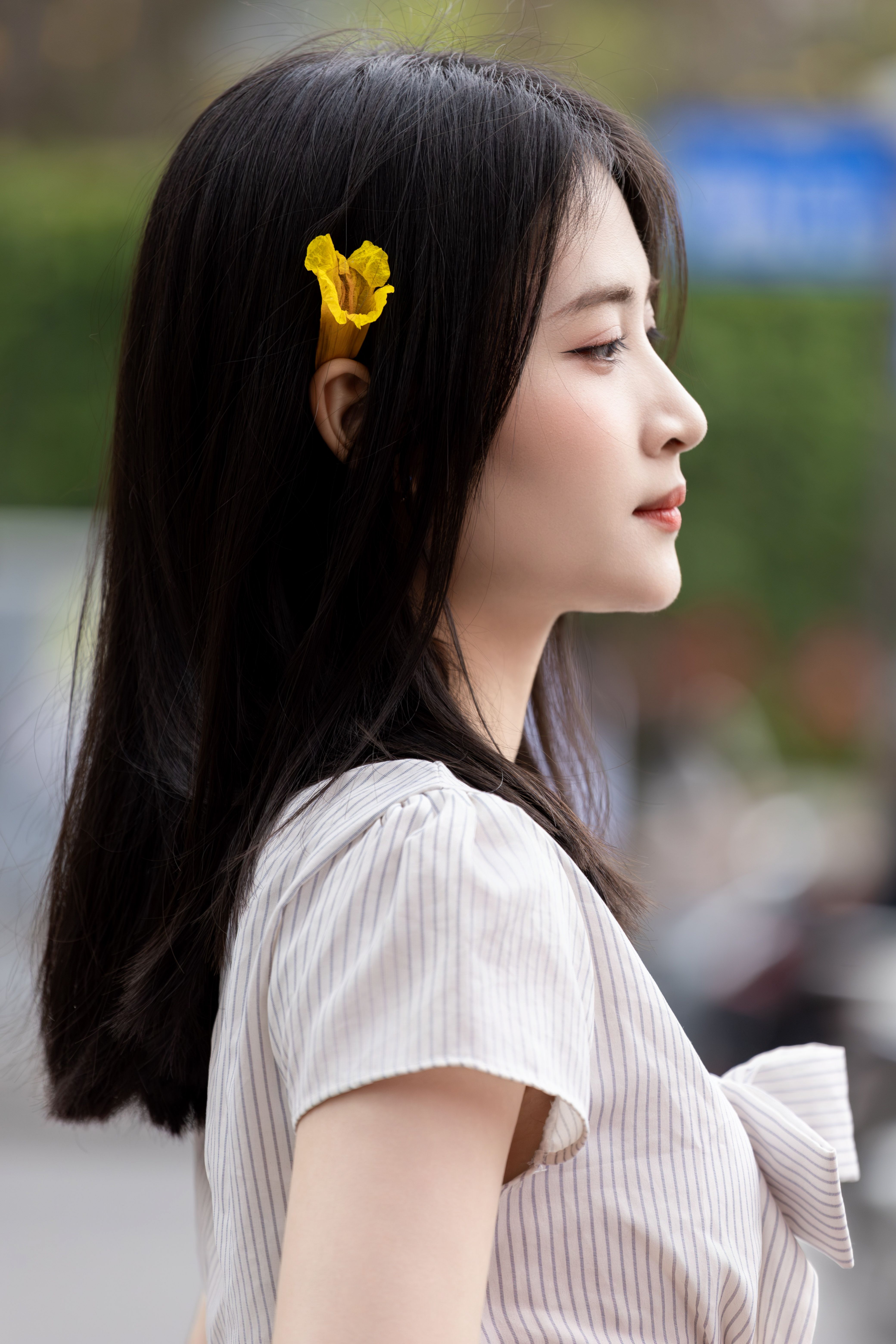 Side profile of a young woman with long hair and a yellow flower, photographed outdoors in Hanoi, Vietnam.