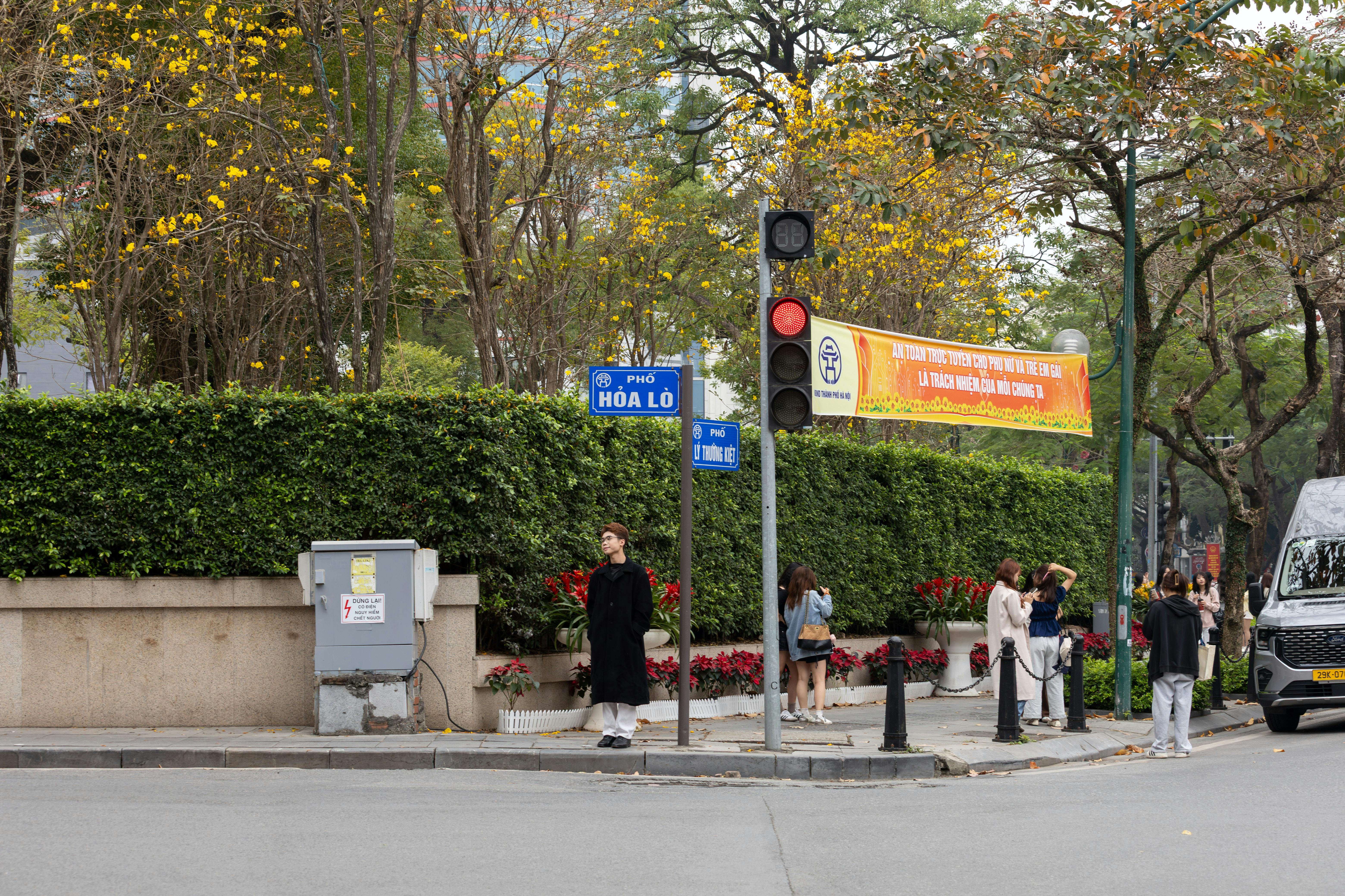 Street scene in Hanoi featuring Hòa Lò street sign and pedestrians, evoking urban and cultural vibes.