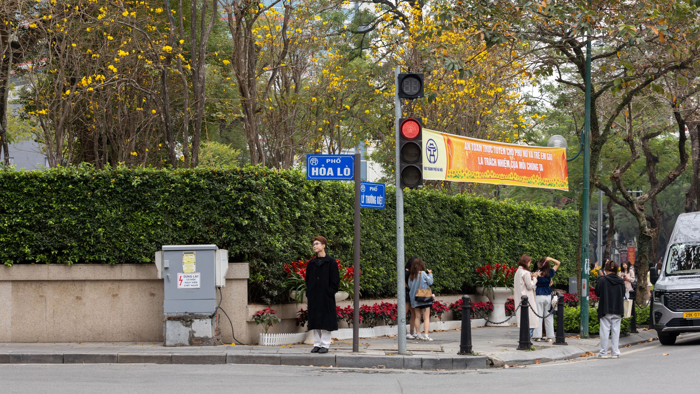 Street scene in Hanoi featuring Hòa Lò street sign and pedestrians, evoking urban and cultural vibes.