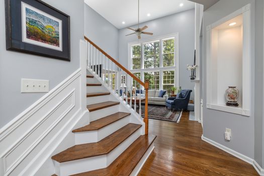 Elegant interior of a living room with staircase, large windows, and decor.