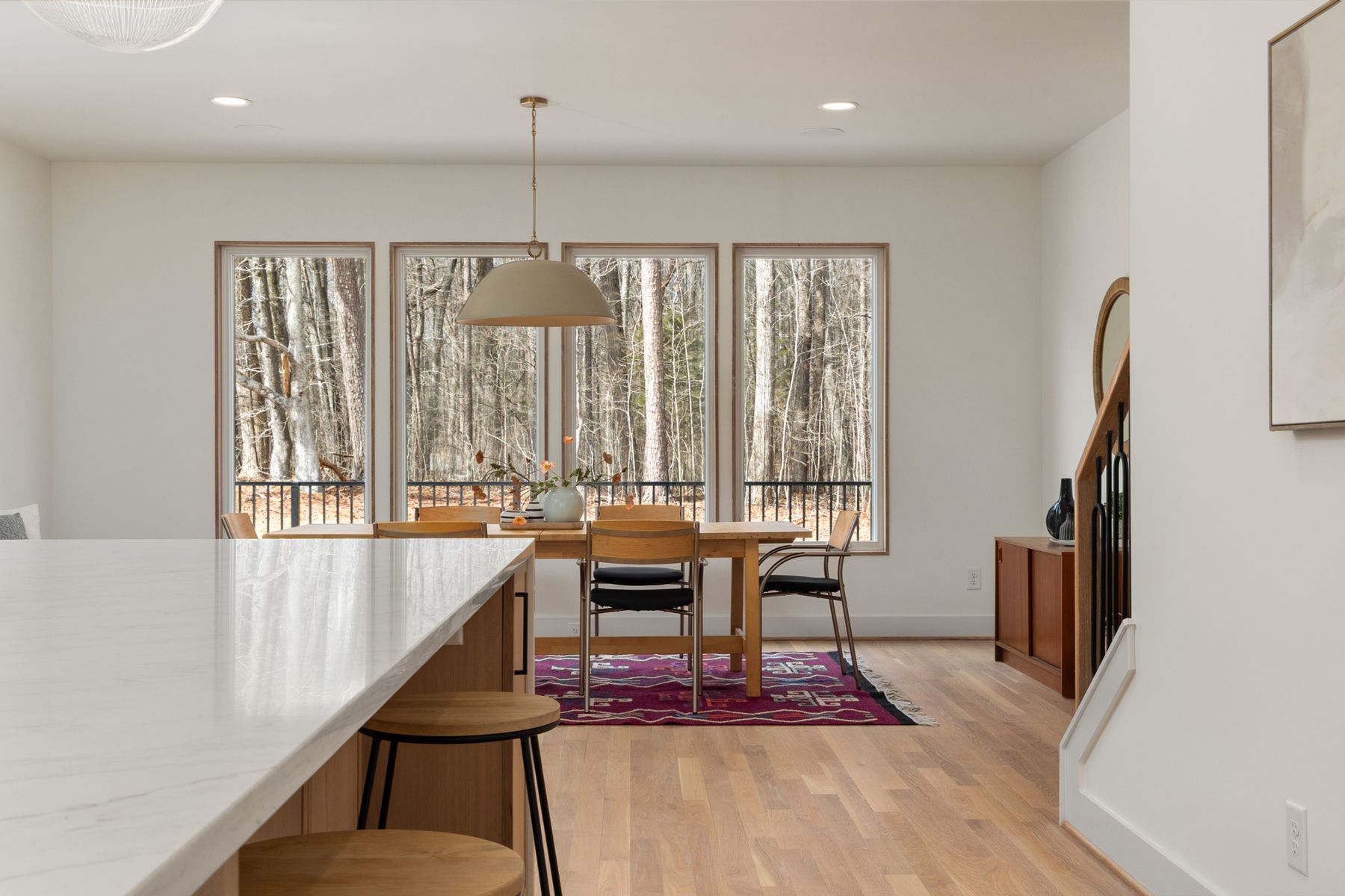 A dining room with a long table and tall windows onto trees