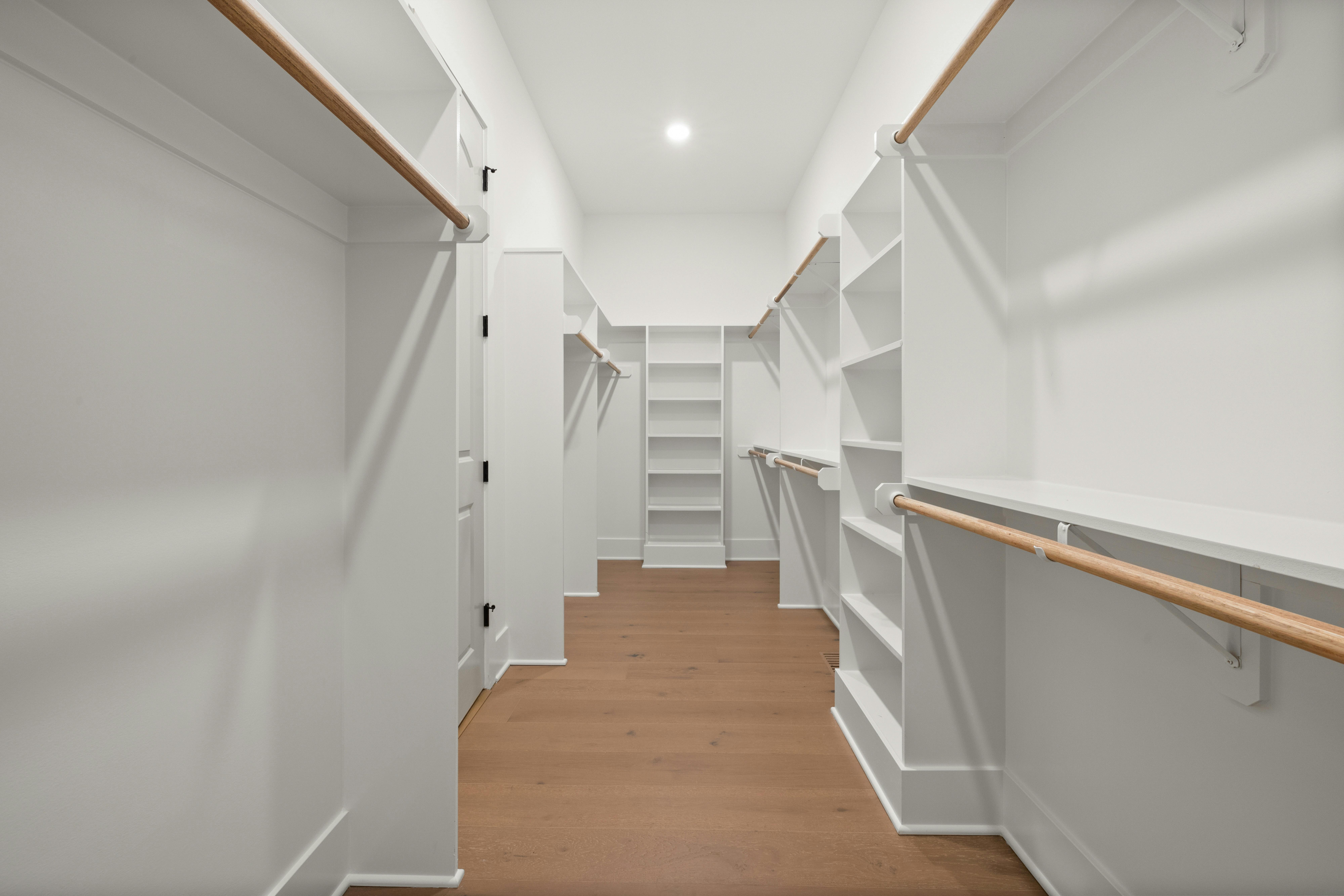 Modern walk-in closet with wooden floors and white shelving units.