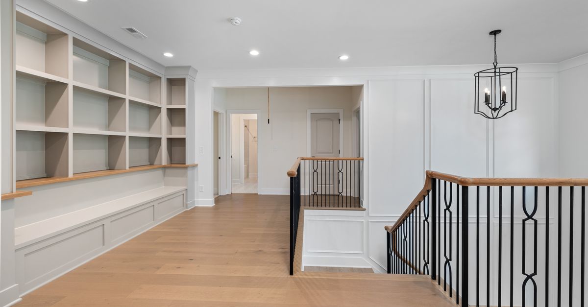 Bright modern foyer featuring wooden floors, custom shelving, and an elegant staircase.