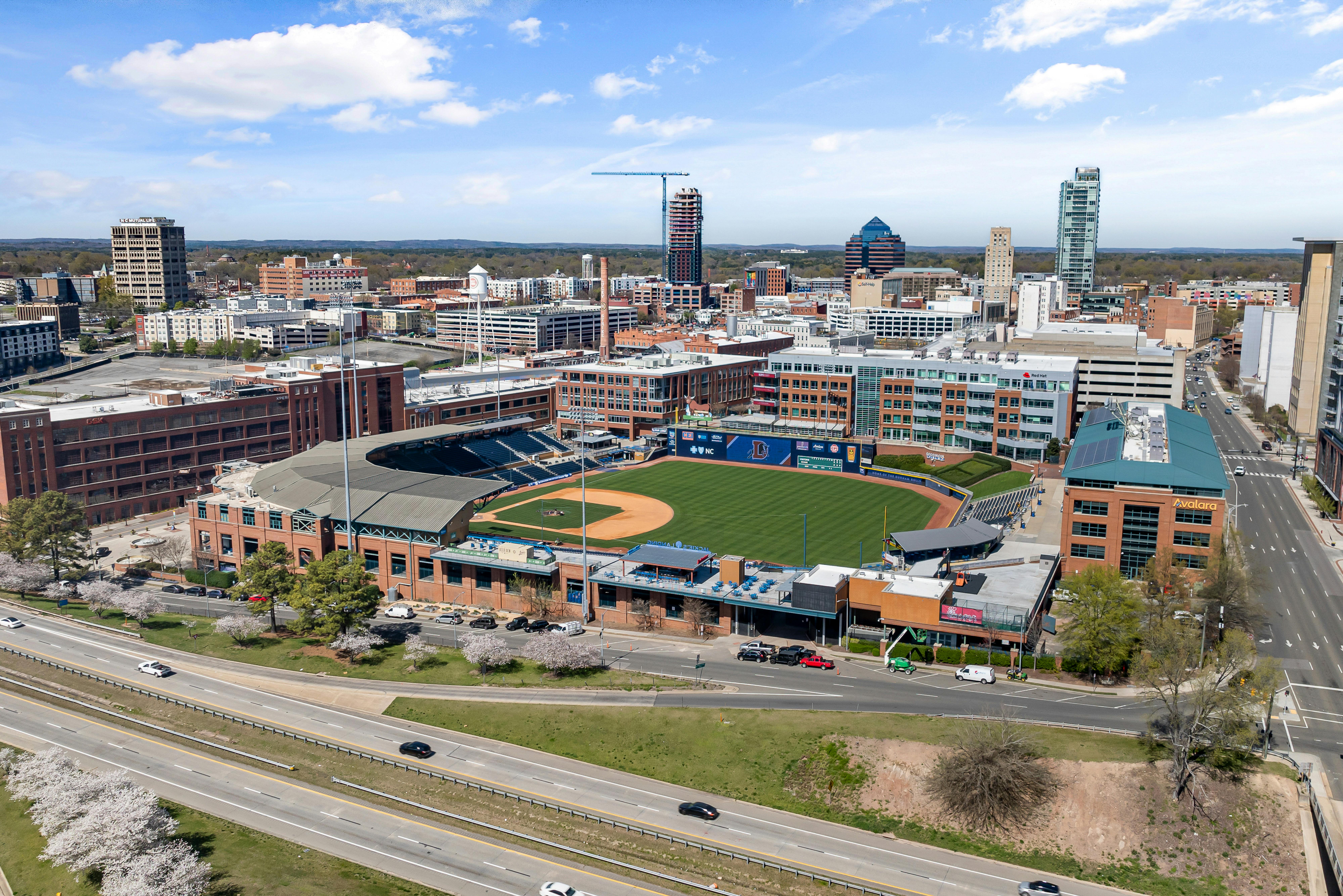Aerial shot of Durham Bulls Athletic Park with city skyline in springtime.