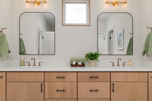 Elegant bathroom featuring double sinks, mirrors, and warm lighting. Modern design with wooden cabinetry.
