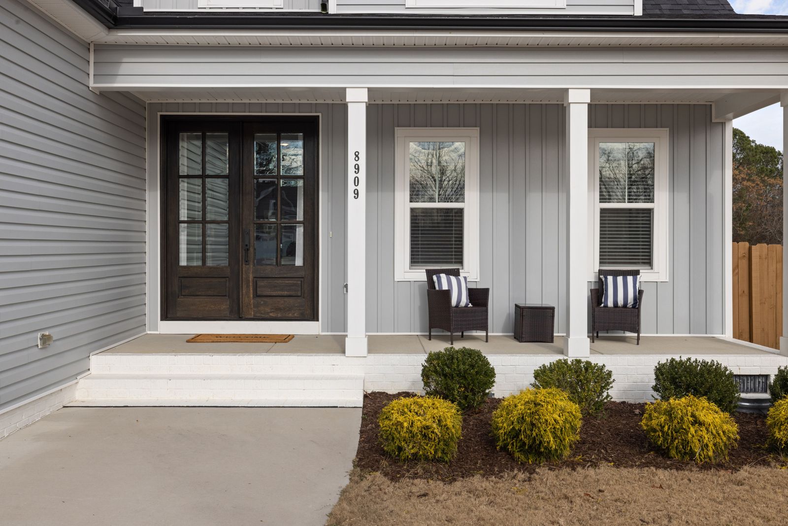 Two-story suburban home with light-colored siding and an inviting covered front porch with seating, framed by neatly kept shrubs, Hobson West, Naperville IL