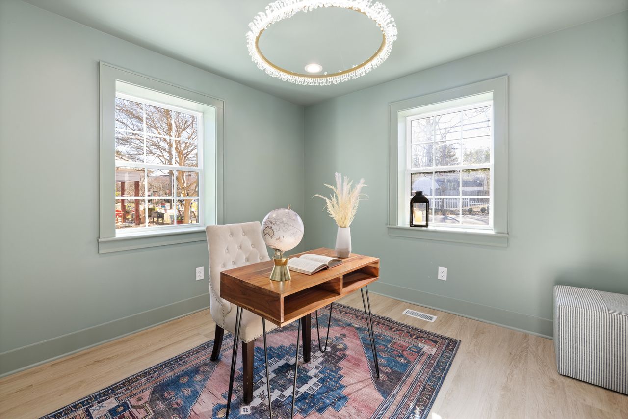 Small home office with soft sage green painted walls, a wooden desk and a vintage-style rug