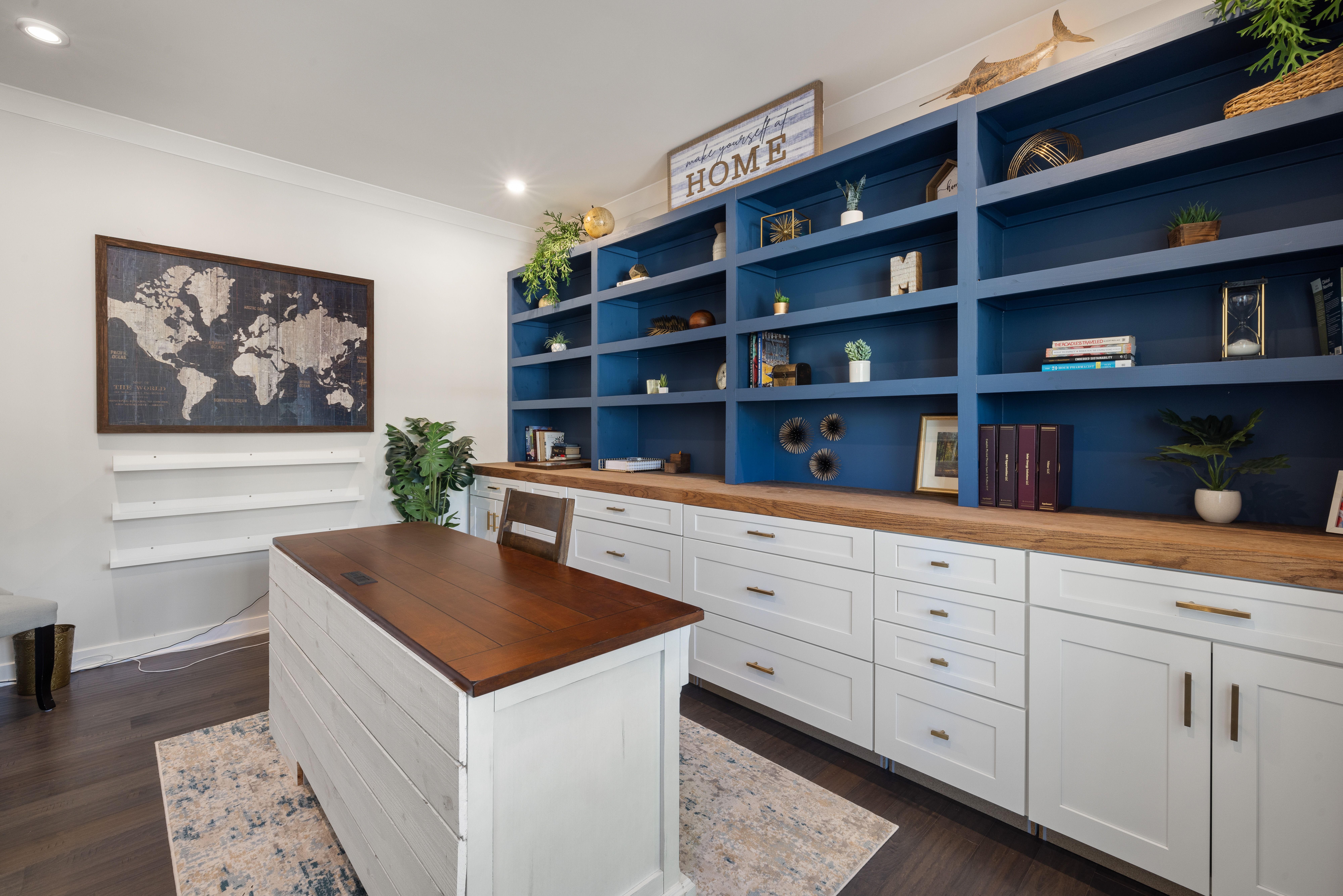 Modern home office featuring blue shelves with decor, a wooden desk, and world map artwork.