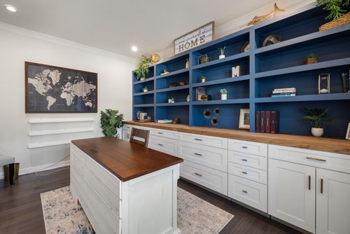 Free Modern home office featuring blue shelves with decor, a wooden desk, and world map artwork. Stock Photo