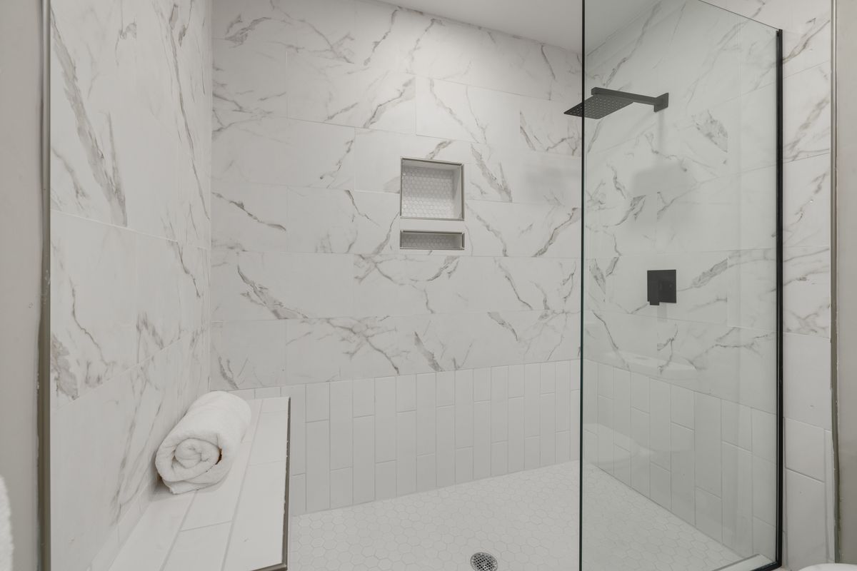White marble-look tiled shower with a frameless glass screen, matte-black shower hardware, recessed niches, a built-in bench and small-format tiled floor.