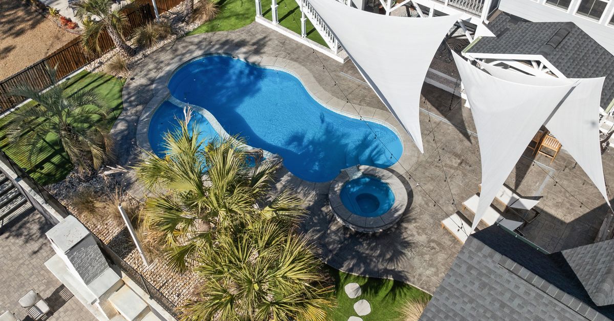 Stunning aerial view of a modern backyard featuring a blue swimming pool, palm trees, and stylish shade sails.