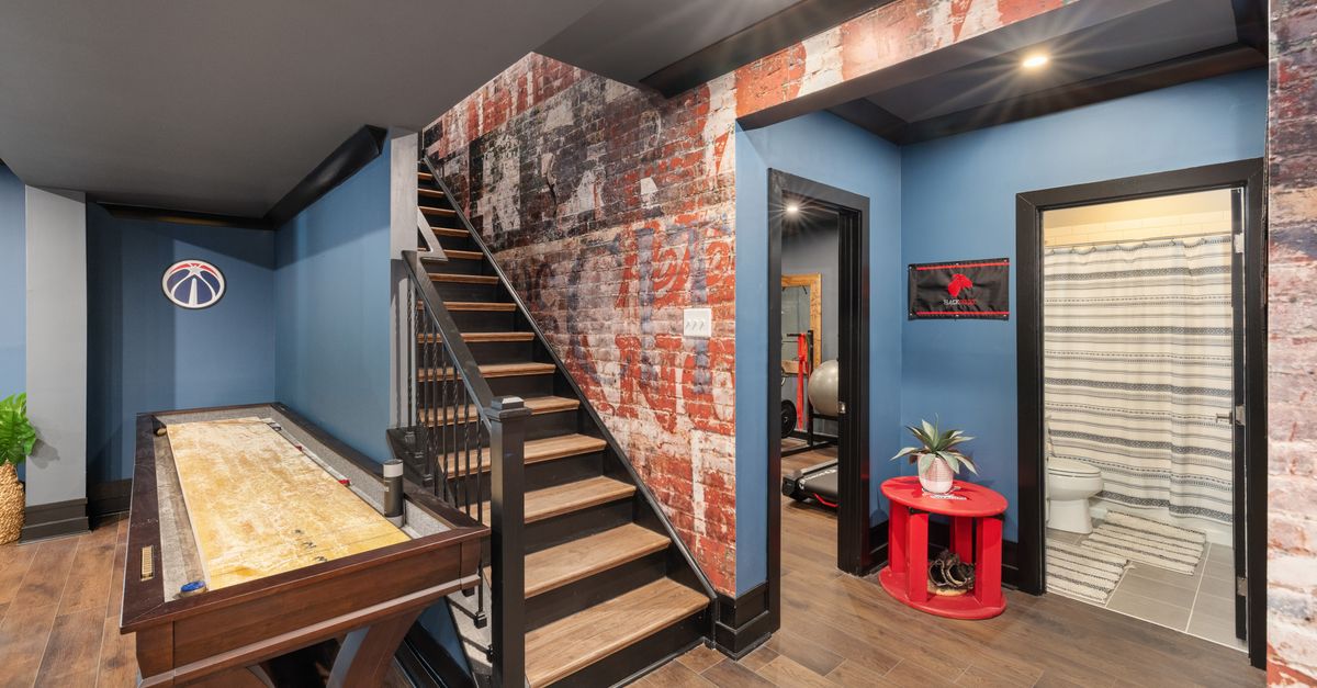 Modern basement interior with game table, rustic brick walls, and a stairway.