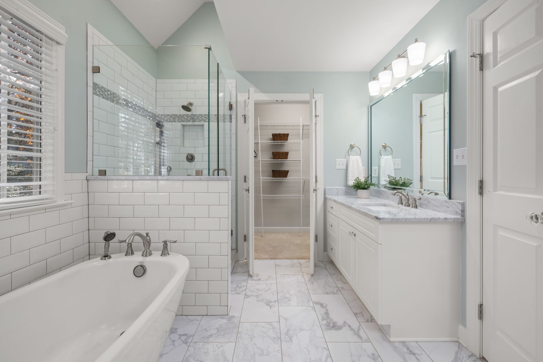 Elegant bathroom with white marble, glass shower, and bright lighting.