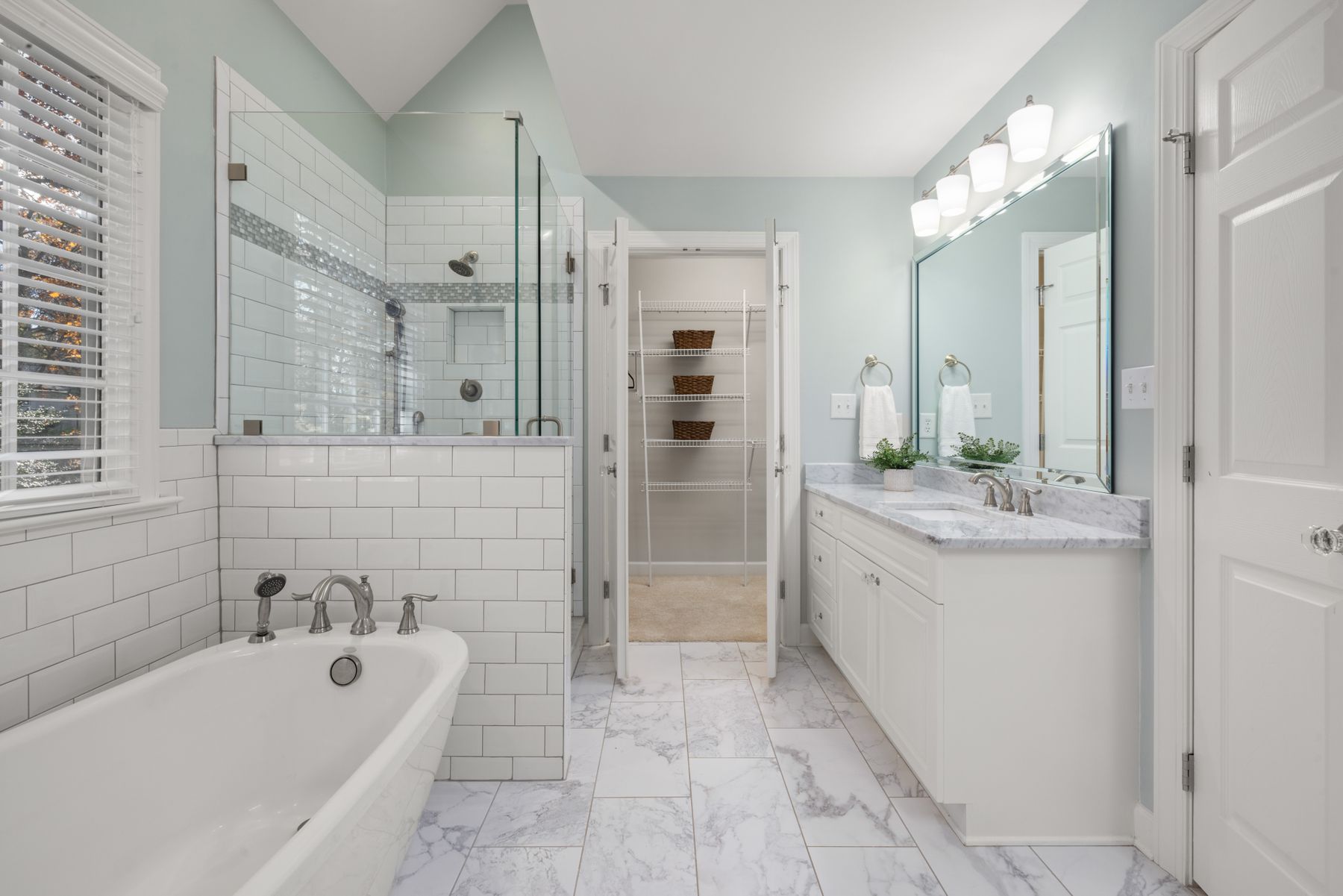 White marble bathroom with glass shower, bright lighting and a mix of polished and softer surfaces