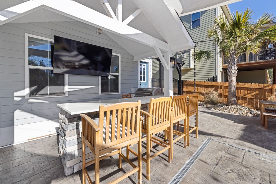 Spacious wooden seating and stone bar under a covered patio with wall-mounted TV by Curtis Adams.