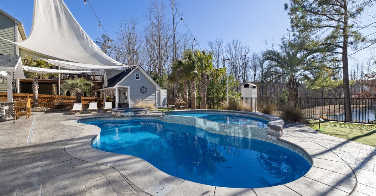 A sunny backyard oasis featuring a luxurious pool, deck, and palm trees, perfect for relaxation.