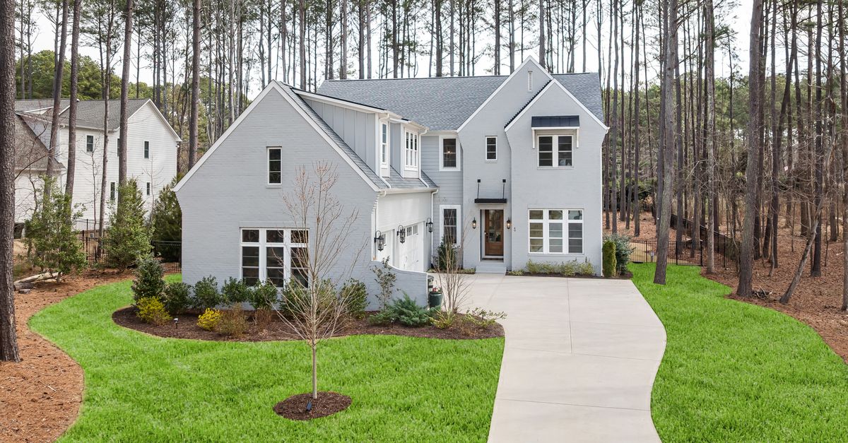 Elegant suburban home with gray siding and spacious driveway set amidst towering pine trees.
