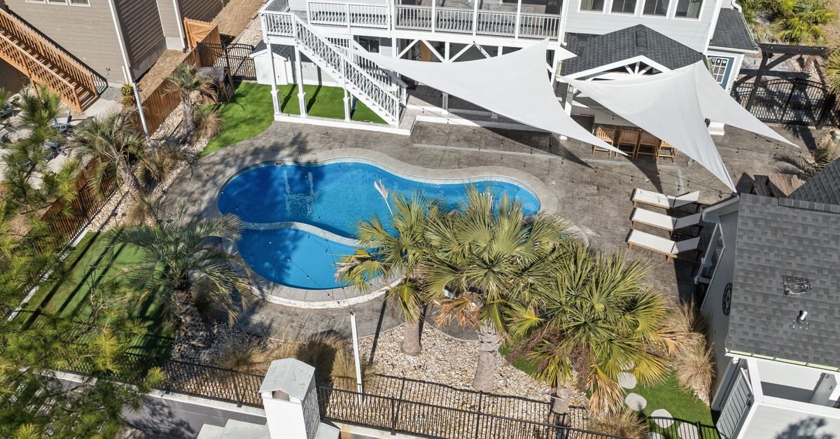 Aerial view of a luxuriously designed backyard with a kidney-shaped pool and palm trees.