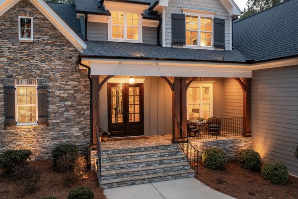 A stone-fronted house with a warmly lit front porch at dusk — photo by Curtis Adams on Pexels