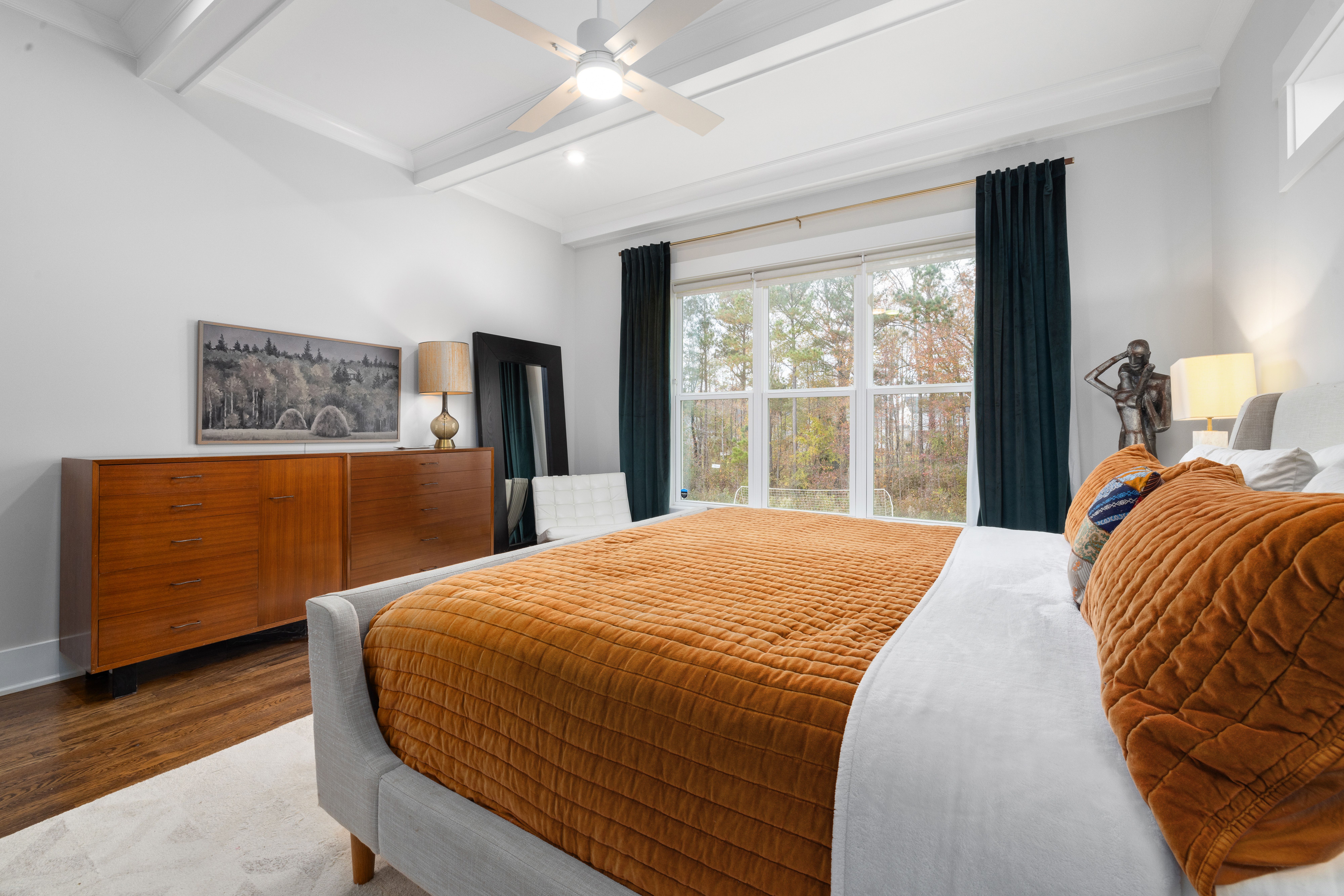 Stylish bedroom interior featuring orange bedding, wooden furniture, and large window view.
