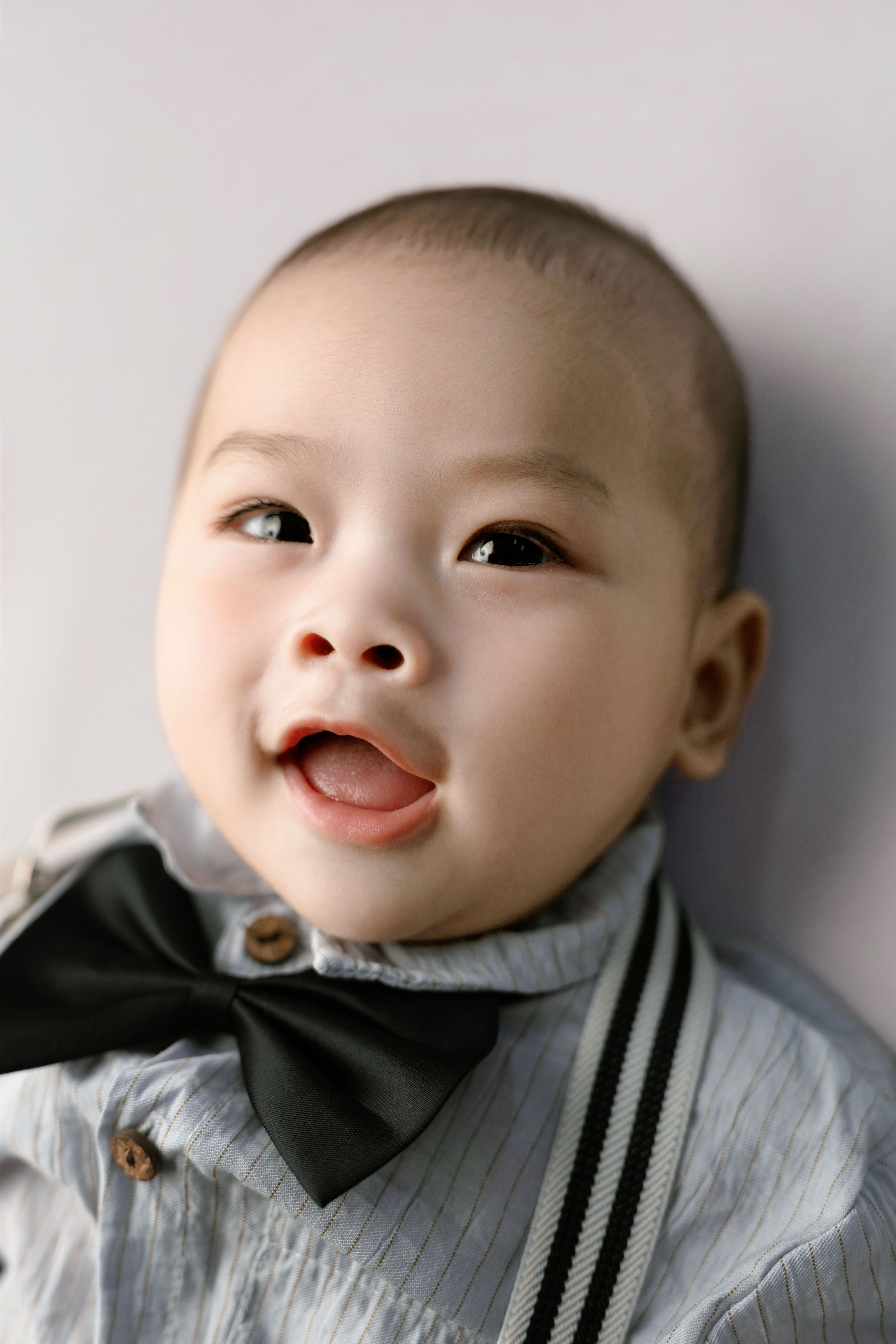 Cute baby in a bowtie smiling joyfully, wearing a button-down shirt.