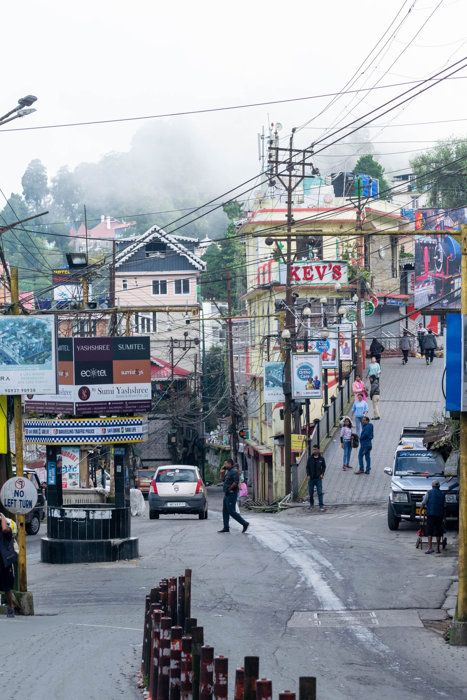 Keventer's corner on a misty Darjeeling morning, its red KEV'S sign above the sloping street and early walkers