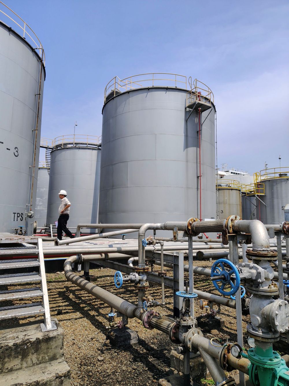 Worker walking beside industrial oil storage tanks
